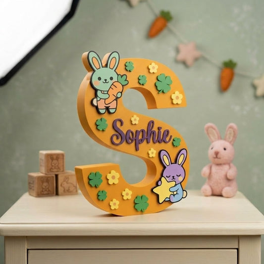 Dekorativer Buchstabe S zum Aufstellen in Senfgelb, personalisiert mit dem Namen Sophie in Lila, verziert mit niedlichen Häschen, Blumen und grünen Kleeblättern in Relief, für die Kinderzimmerdekoration.