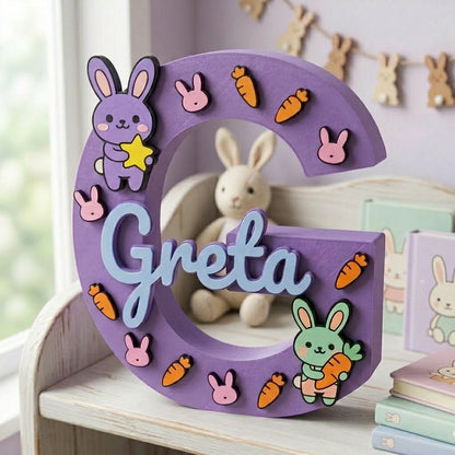 Lila dekorativer 3D-Buchstabe G personalisiert mit dem Namen Greta in Blau. Kinderzimmerdekoration mit Hasen-Thema, in Relief zusammen mit Karotten und einem gelben Stern aufgebracht.