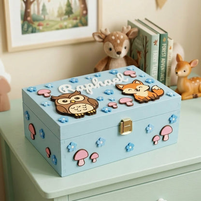 Erinnerungsbox aus hellblauem Holz, für einen Jungen personalisiert mit dem Namen Raphael, verziert mit 3D-Applikationen im Waldtier-Motiv, darunter eine Eule, ein Fuchs, rosa Pilze und blaue Blumen.