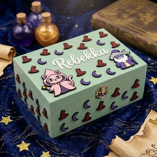 Hellgruene personalisierte Holzbox mit dem Namen Rebekka in Relief, dekoriert mit 3D-Applikationen zum Zauberthema: Katze mit Umhang, Zauberer, violette Monde und bordeauxrote Hexenhuete, mit Metallverschluss.