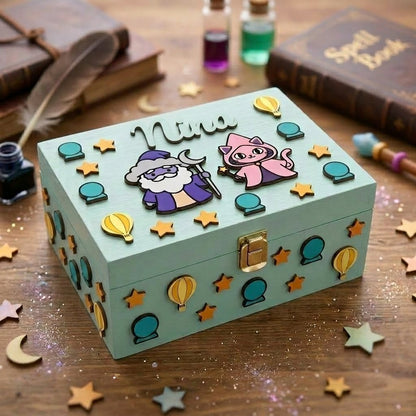 Blaue personalisierte Holzbox mit dem Namen Nina in Relief, dekoriert mit 3D-Applikationen zum Zauberthema, darunter ein Zauberer, eine magische Katze, Sterne, Heissluftballons und Kristallkugeln.