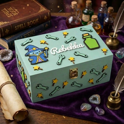 Personalisierte Erinnerungsbox aus Holz mit dem Namen Rebekka in Relief. Wassergruenes Kaestchen mit 3D-Dekorationen zum magischen Fantasy-Thema: kleiner Zauberer, Zaubertrank-Flaeschchen, Sterne und Schraubenspluesseln. Hintergrund mit violettem Samt, Zauberspruchbuechern, Kristallen und Federn.