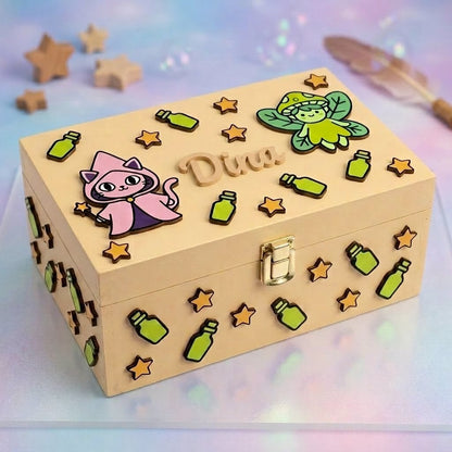 Personalisierte Erinnerungsbox aus Holz mit dem Namen Dina in Relief, zum Zauber-Thema dekoriert mit Reliefapplikationen: Zauberkatze mit rosa Umhang, gruene Fee, Zaubertrank-Flaeschchen und Sternchen. Goldener Frontverschluss aus Metall.