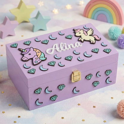 Erinnerungsbox aus fliederfarbenem Holz, personalisiert mit dem Namen Alina als weißes Relief, dekoriert im Einhorn-Stil mit Diamanten, Monden und goldenem Verschluss vorne.