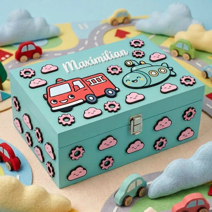 Personalisierte Erinnerungsbox aus hellblauem Holz für Kinder mit dem Namen Maximilian, dekoriert mit 3D-Reliefapplikationen eines roten Feuerwehrautos, eines U-Boots, lächelnder rosa Wölkchen und Zahnräder.
