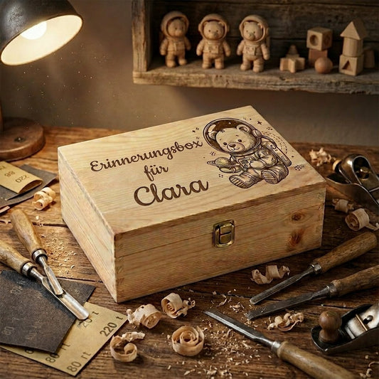 Personalisierte Erinnerungsbox aus Holz mit Lasergravur des Namens Clara und einem Astronautenteddybären, auf einem Handwerkertisch mit Tischlerwerkzeug und Holzspänen.