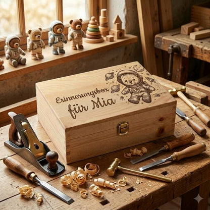 Personalisierte Holz-Erinnerungsbox mit dem Namen Mia und der Gravur eines Astronautenteddybären mit Planeten-Motiv, auf einer Zimmermannswerkbank mit Tischlerwerkzeug und Holzspänen.