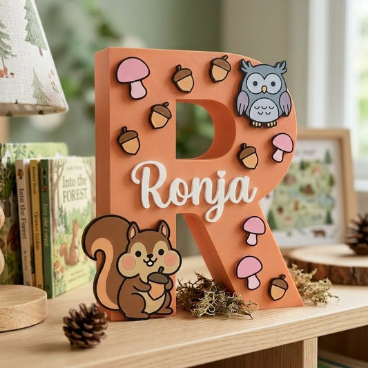 Dekorativer personalisierter Buchstabe R mit dem Namen Ronja. 3D-Initiale in Pfirsichfarbe mit Waldthema fürs Kinderzimmer, mit erhabenen Applikationen von Eichhörnchen, Eule, Eicheln und rosa Pilzen.