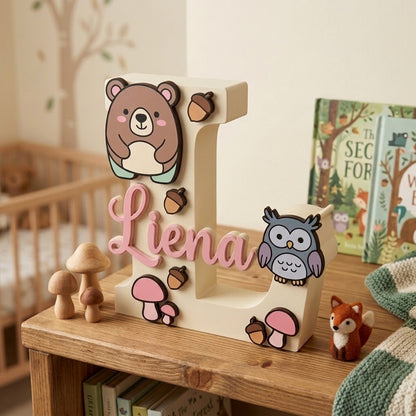 Holzbuchstabe L personalisiert mit dem Namen Lena in rosa Kursivschrift, Kinderzimmerdekoration mit Waldmotiv und erhabenen Details von Bär, Eule, Pilzen und Eicheln.