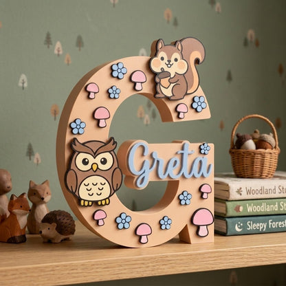 Holzbuchstabe G personalisiert mit dem Namen Greta, Kinderzimmerdekoration mit Waldthema und 3D-Applikationen aus Eule, Eichhörnchen, rosa Pilzen und blauen Blumen.