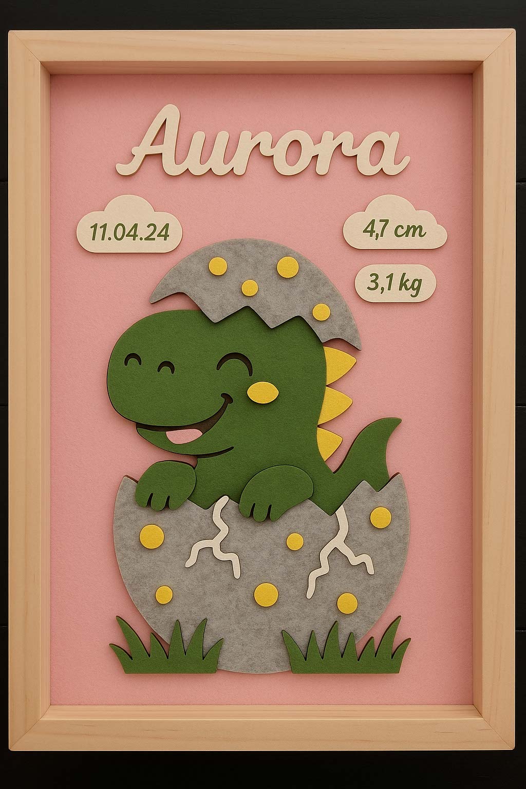 Geburtsbild mit grünem Dinosaurier aus Filz, der aus dem Ei schlüpft, Name Aurora auf rosa Grund, Holzrahmen