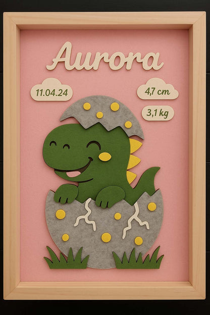 Geburtsbild mit grünem Dinosaurier aus Filz, der aus dem Ei schlüpft, Name Aurora auf rosa Grund, Holzrahmen