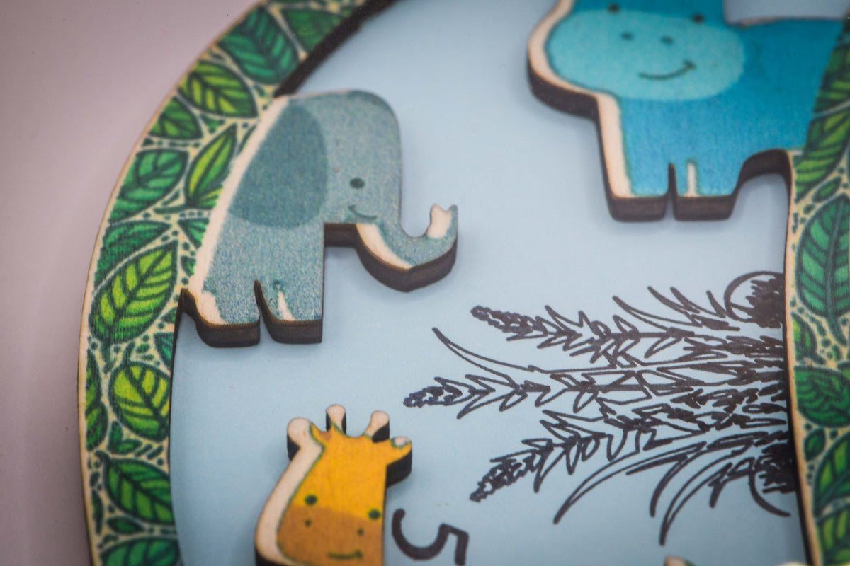 Nahaufnahme der Holztiere auf dem Buchstaben: Elefant, Nilpferd und Giraffe auf hellblauem Grund mit Blätterrand
