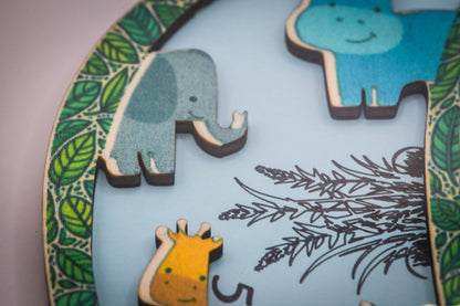 Nahaufnahme der Holztiere auf dem Buchstaben: Elefant, Nilpferd und Giraffe auf hellblauem Grund mit Blätterrand